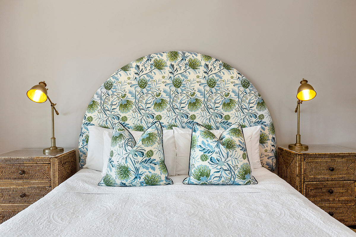 Utopia Goods: bedroom with curved floral headboard, matching pillows, wicker nightstands, and brass table lamps
