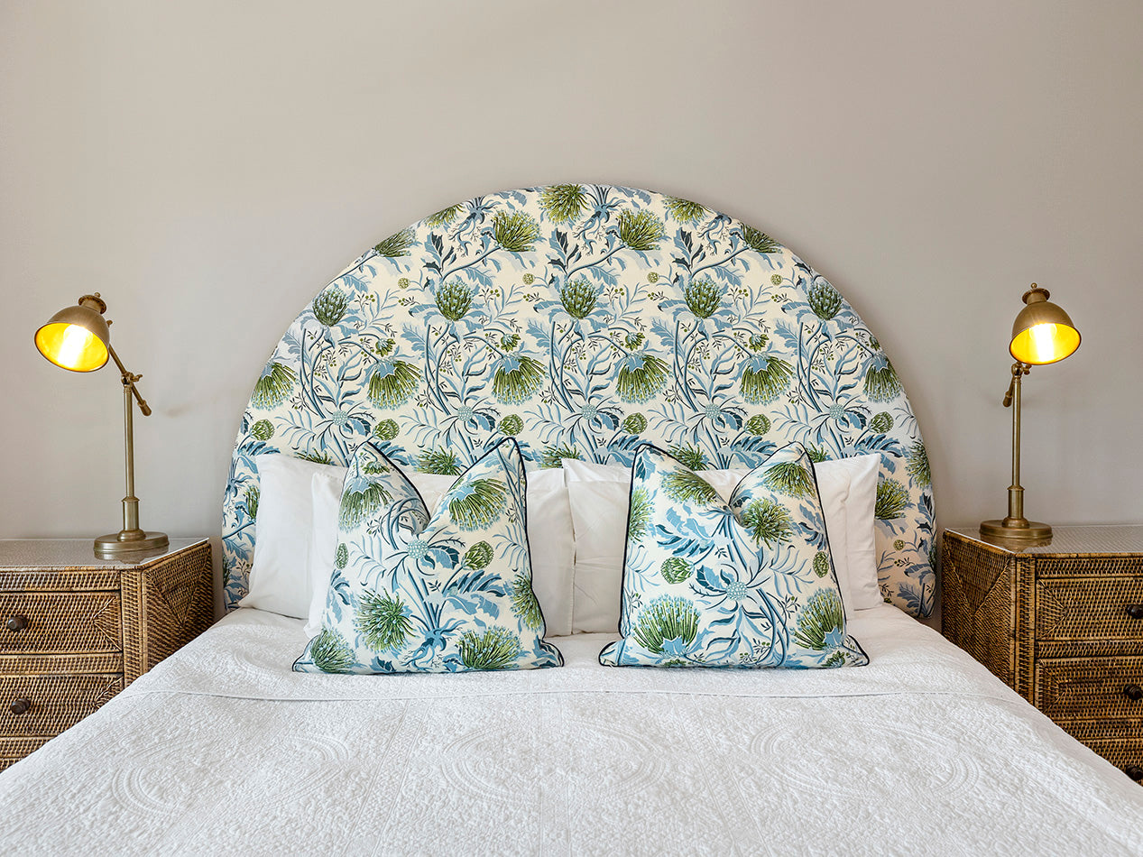 Utopia Goods: bedroom with curved floral headboard in blue and green pattern, matching pillows, and brass bedside lamps
