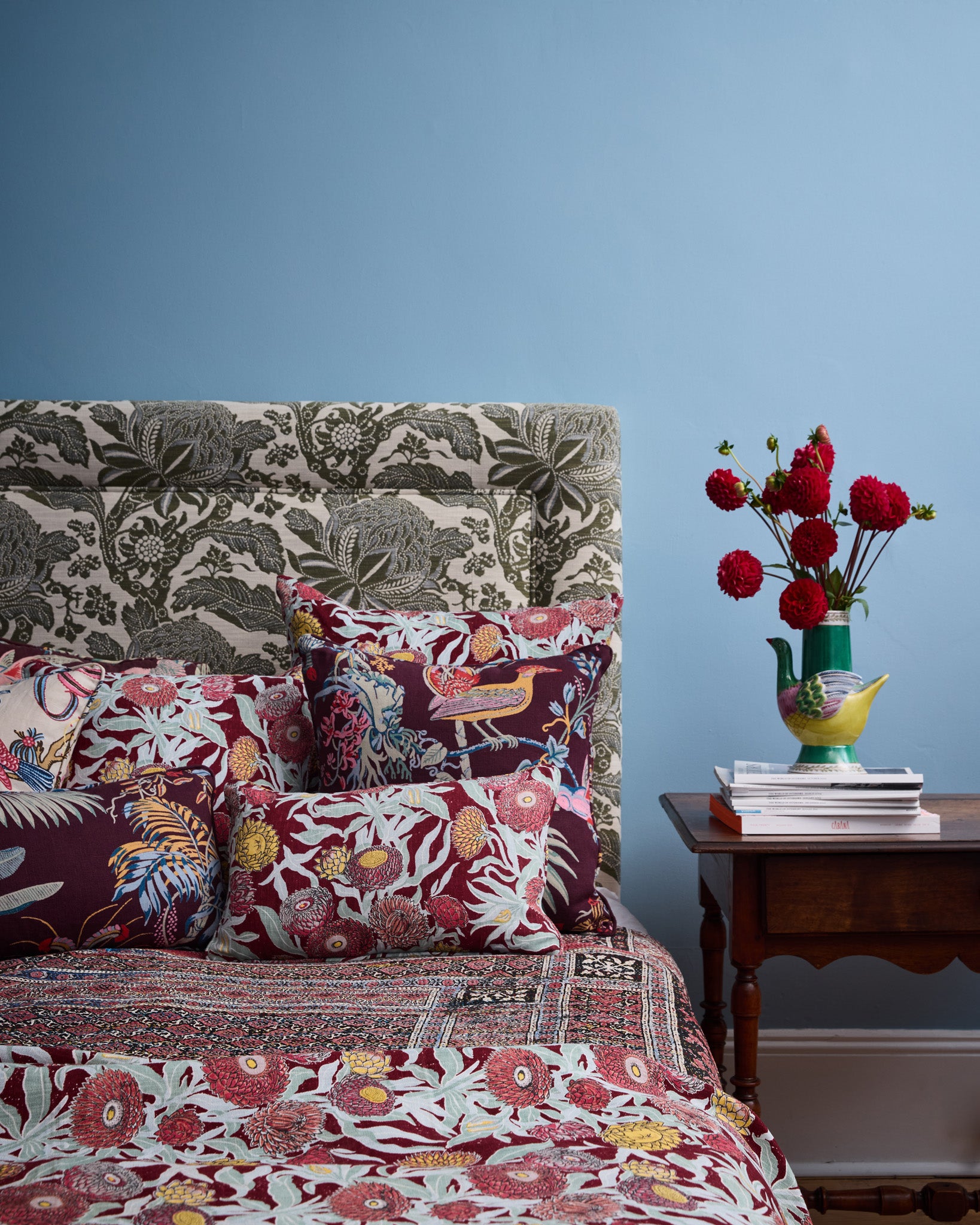 Utopia Goods: bedroom with floral patterned headboard, colorful bedding, and red flowers in vase on wooden nightstand