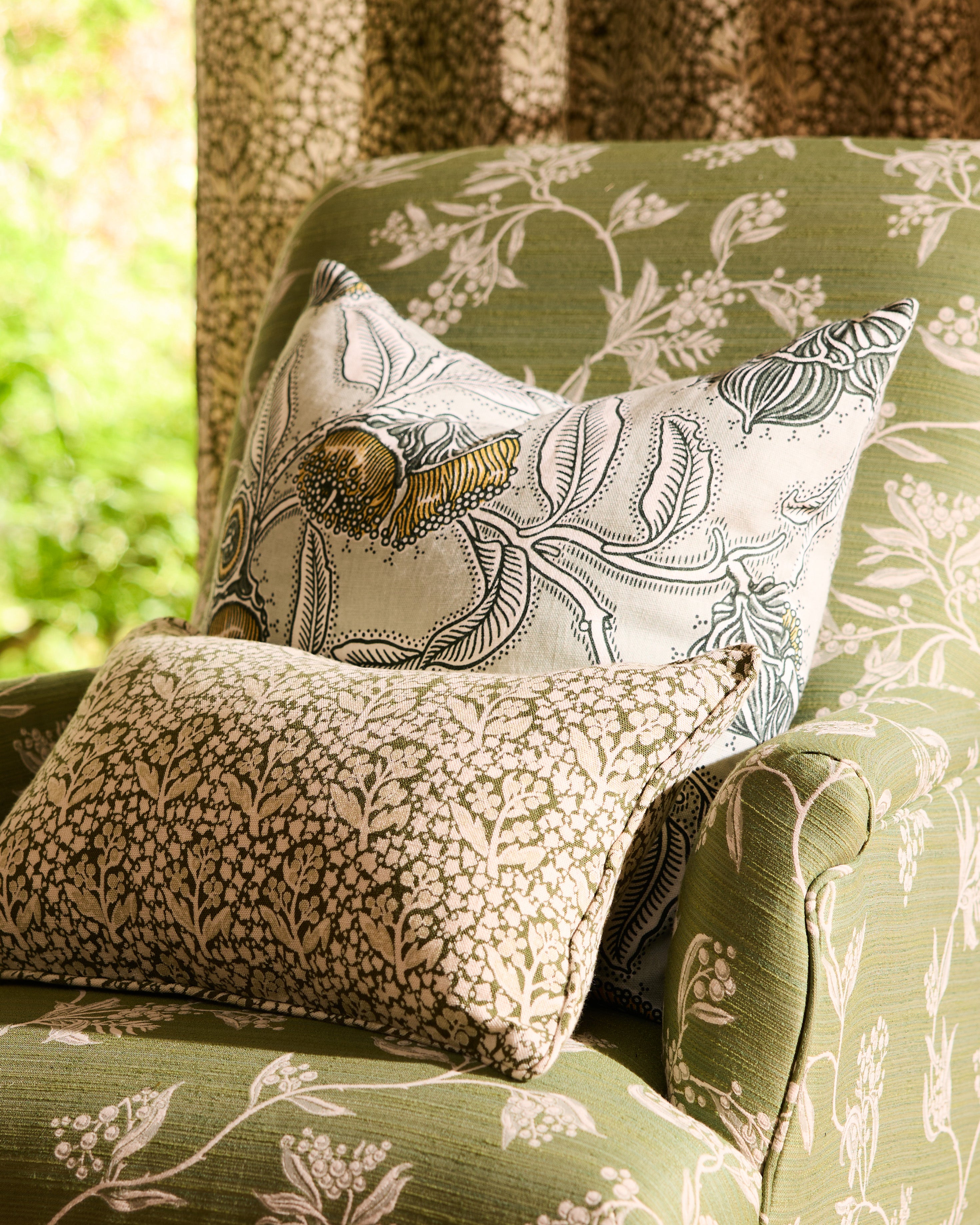 Utopia Goods: Green floral upholstered armchair with decorative throw pillows featuring botanical and geometric patterns