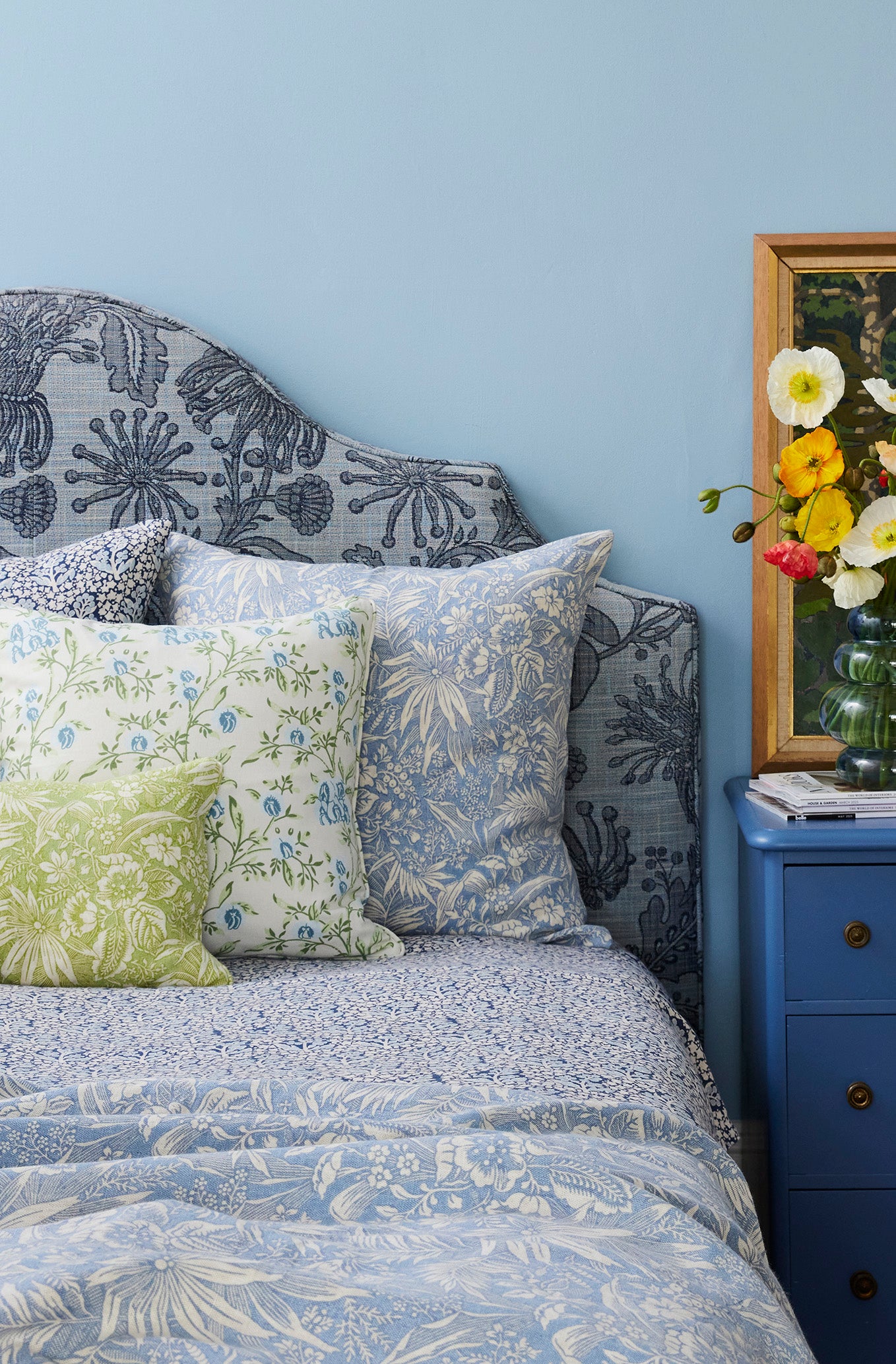 Utopia Goods: blue floral patterned chair with decorative pillows next to blue nightstand with flower vase