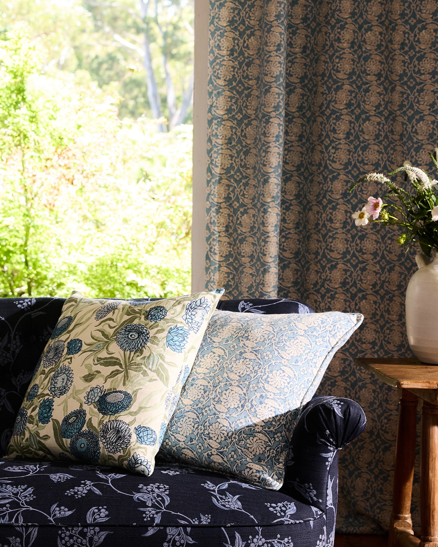 Utopia Goods: dark floral sofa with patterned pillows near window with matching curtains and side table with vase