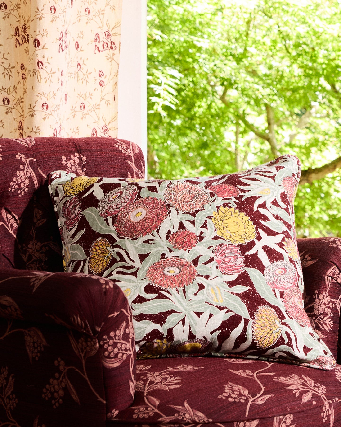 Utopia Goods: floral throw pillow on burgundy patterned sofa near window with green foliage visible outside