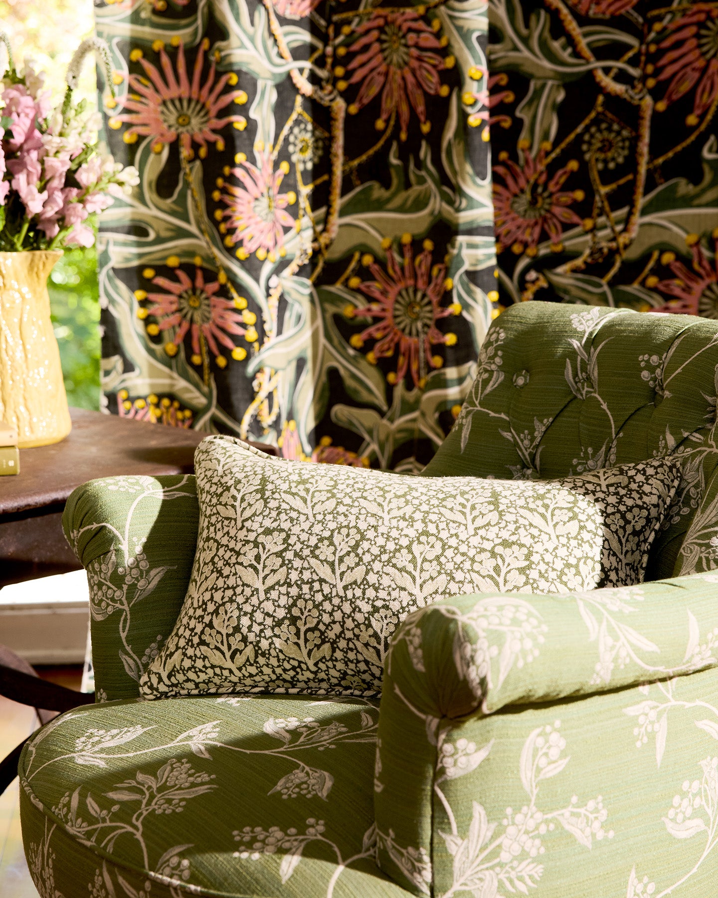 Utopia Goods: green floral patterned armchair with decorative pillows against colorful botanical wallpaper