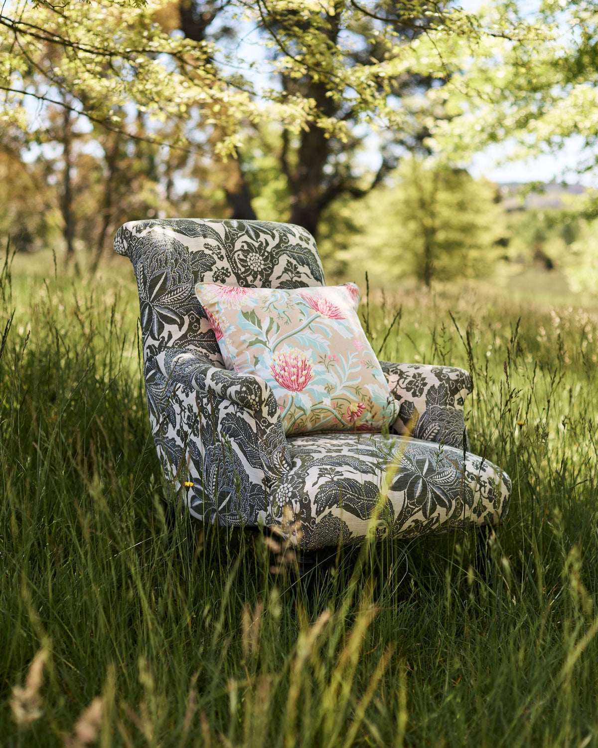Utopia Goods Matchstick Banksia Earth Medium Cushion Cover: floral cushion on patterned armchair in tall grass meadow setting