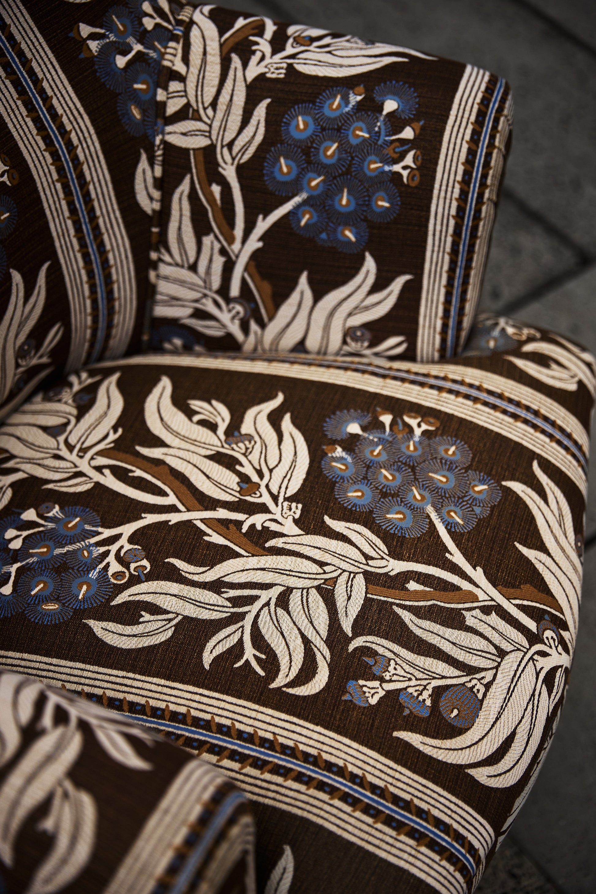 Utopia Goods: close-up of upholstered chair with dark floral fabric featuring blue flowers and cream leaves