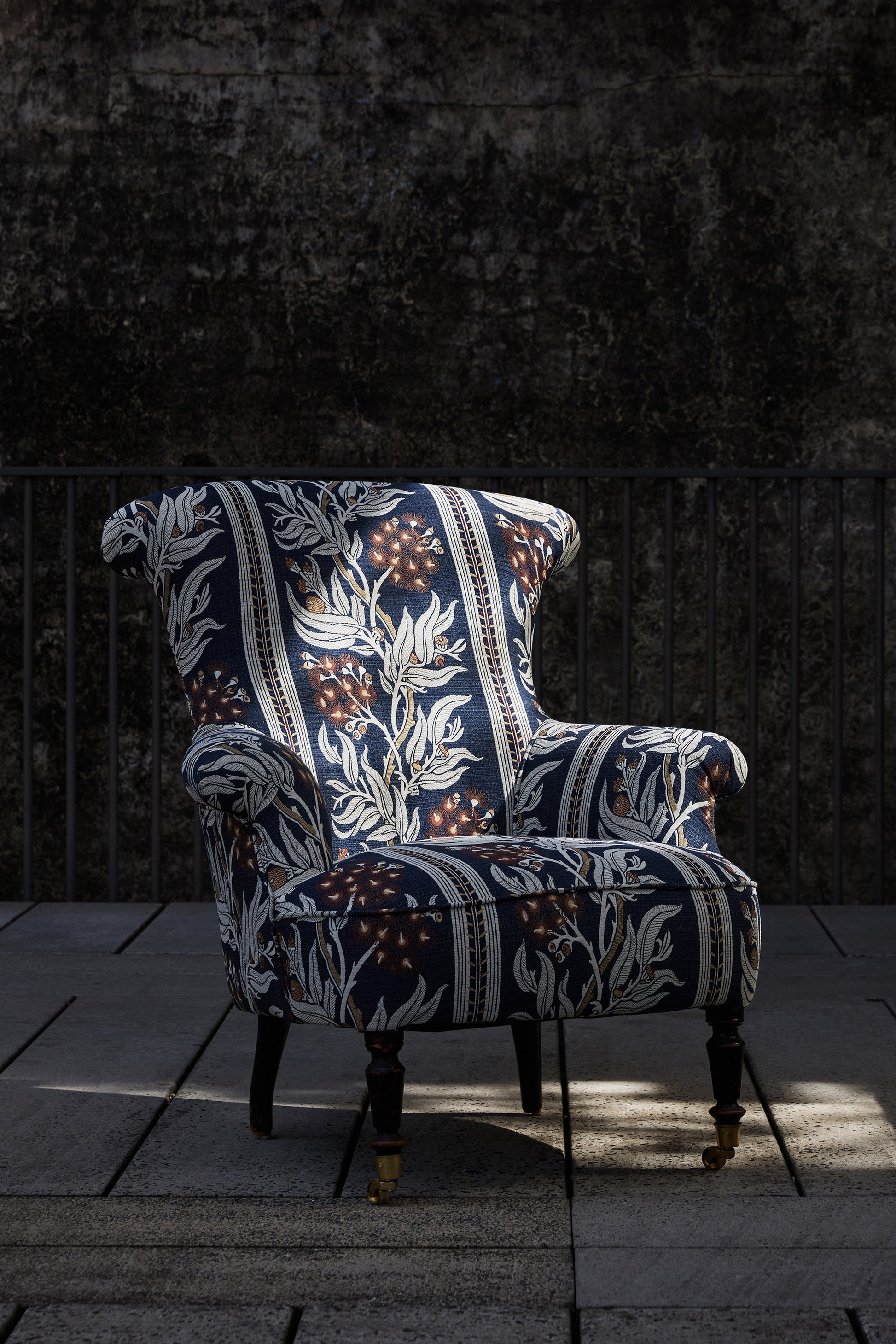 Utopia Goods: ornate wingback chair with blue floral patterned upholstery on stone floor against dark textured wall