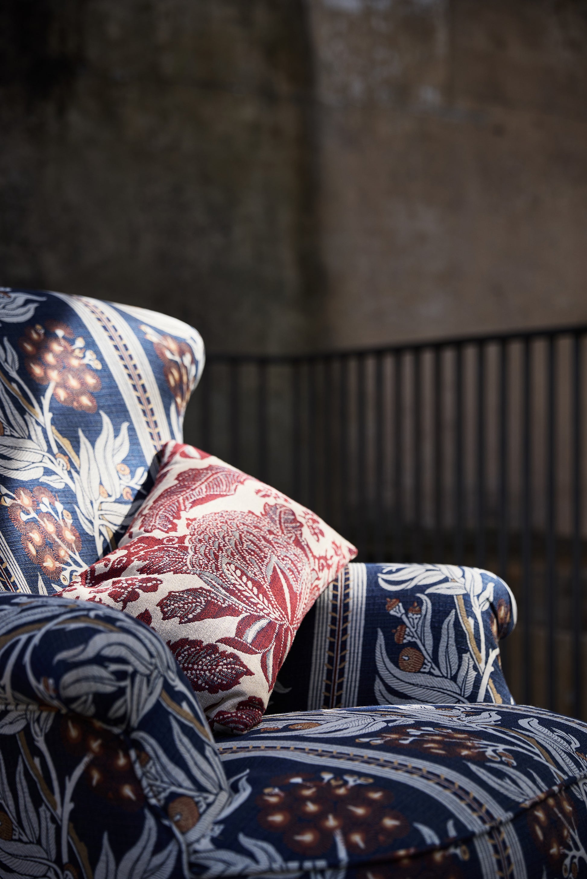 Utopia Goods: upholstered armchair with blue floral fabric and red patterned throw pillow in rustic interior setting