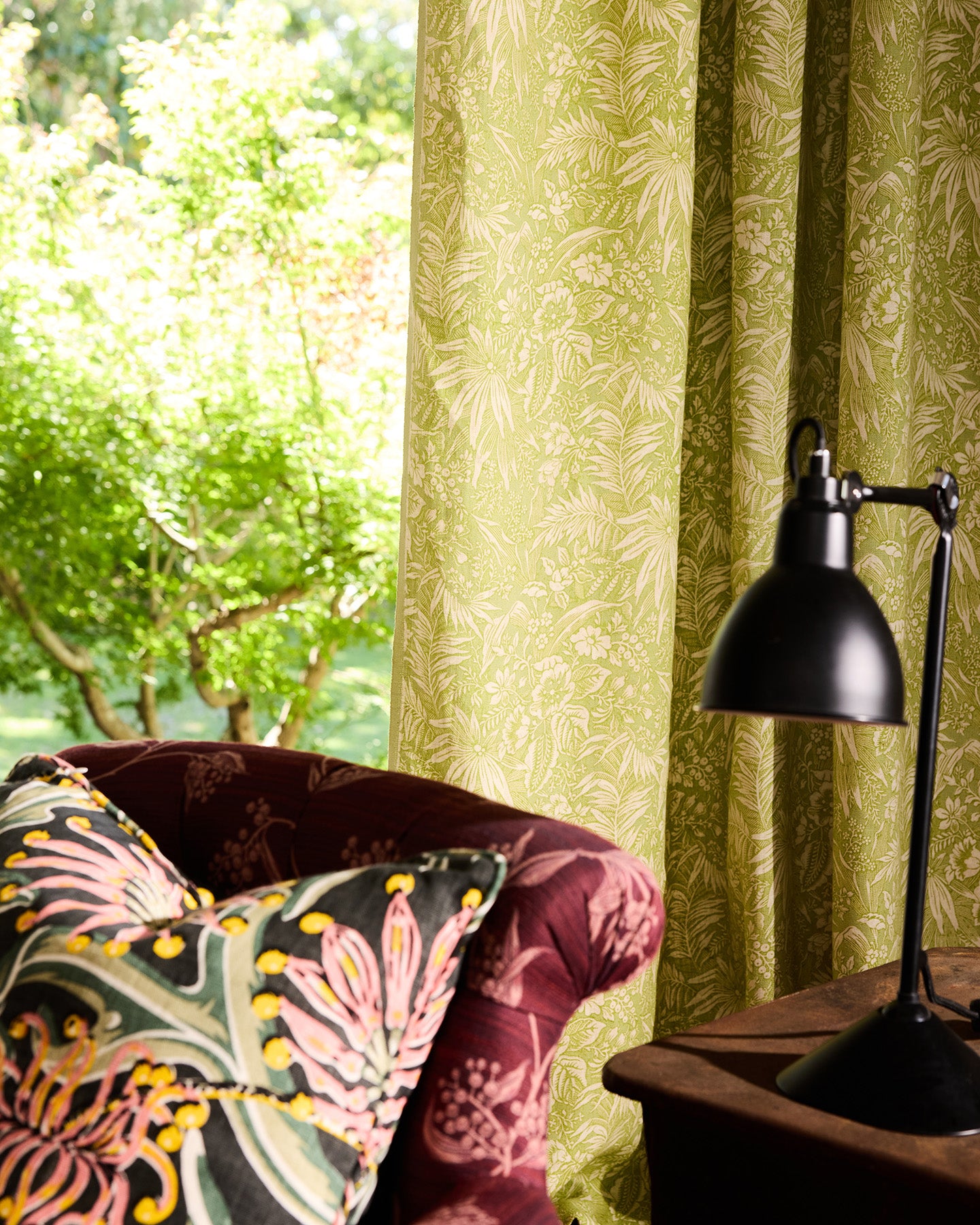 Utopia Goods Palm Grove Green Furnishing Linen: green botanical wallpaper with tropical leaf pattern behind burgundy velvet chair