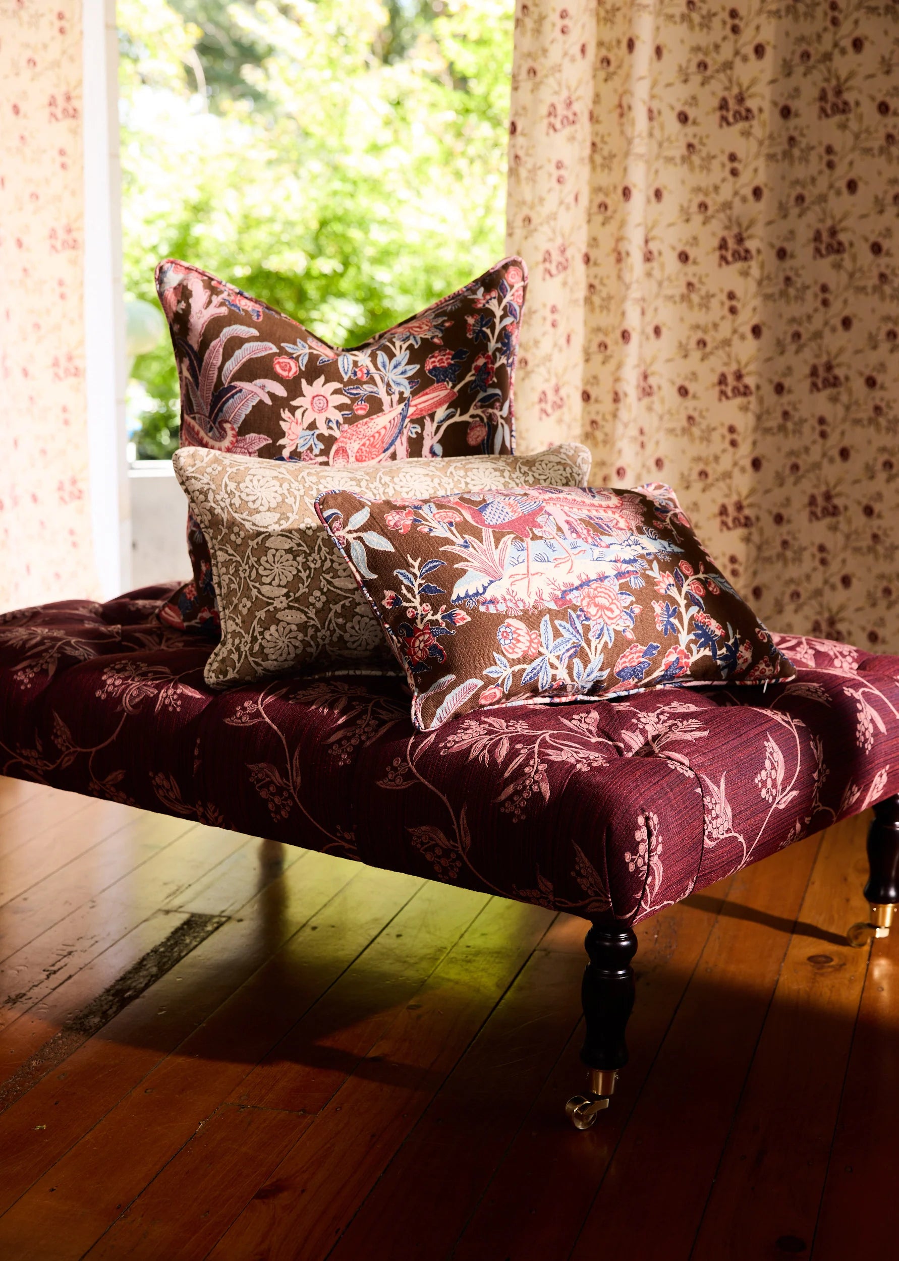 Utopia Goods: ornate burgundy chaise lounge with floral throw pillows by window with patterned wallpaper and wood floors