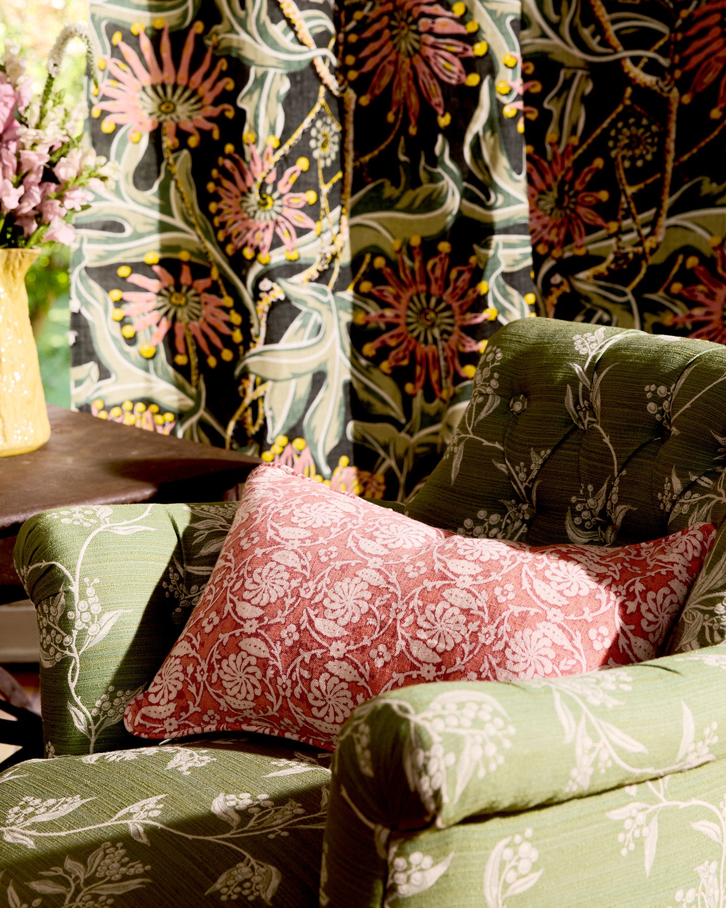 Utopia Goods: green floral armchair with red patterned pillow against dark botanical wallpaper in styled living room