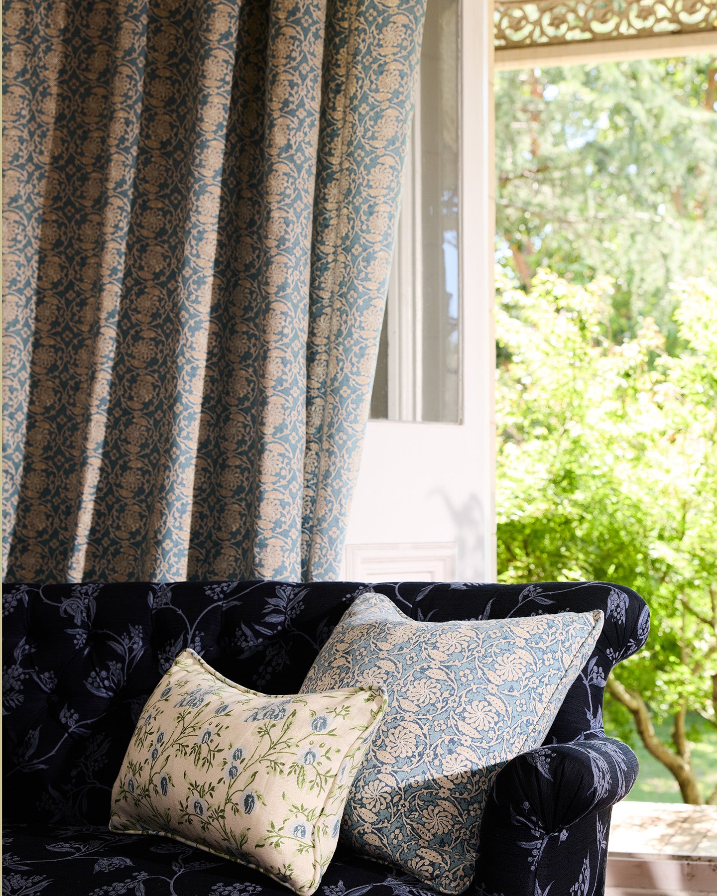 Utopia Goods: Navy patterned armchair with decorative pillows next to matching curtains and bright window view