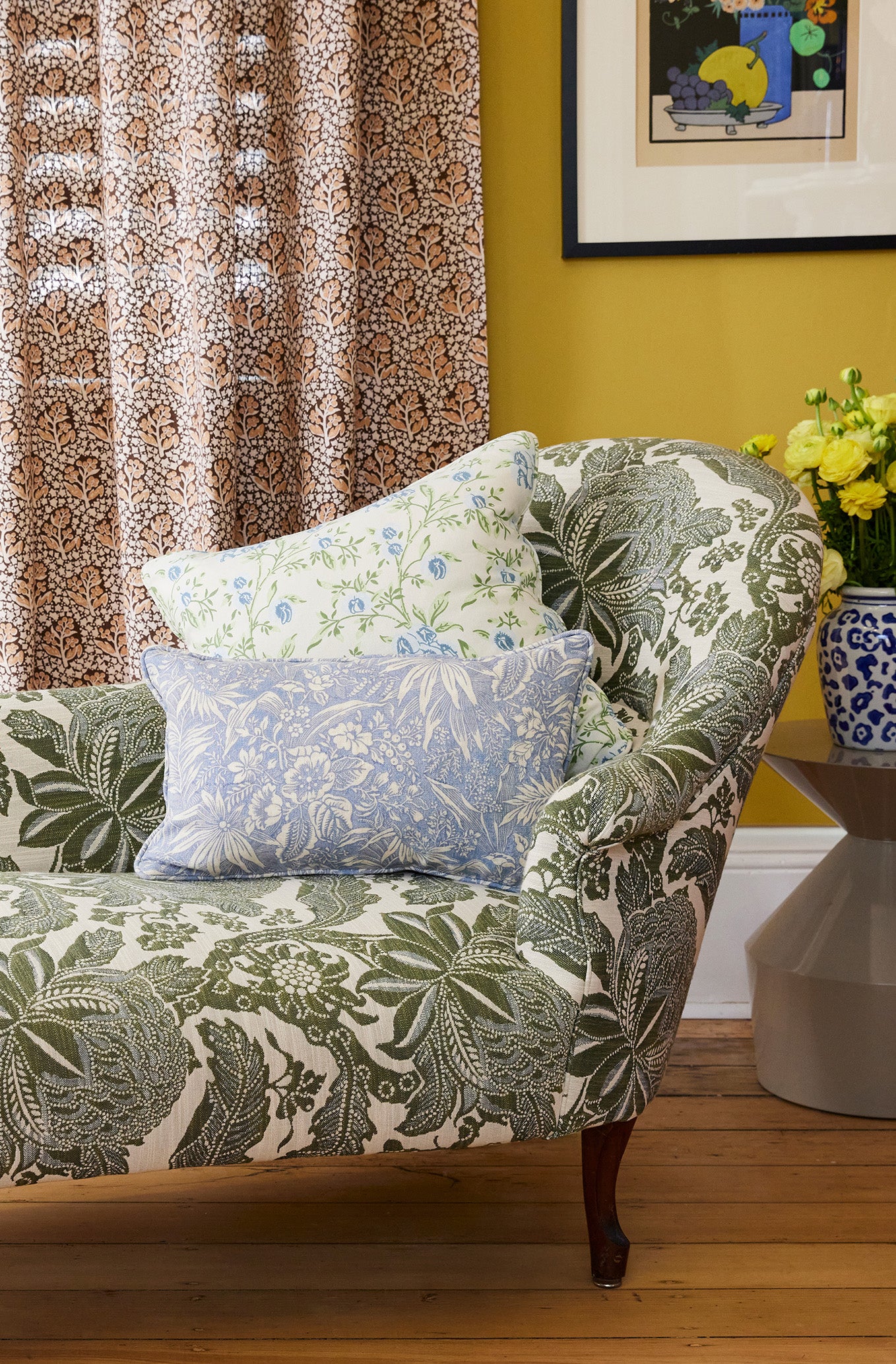 Utopia Goods: floral patterned armchair with decorative pillows in room with yellow walls and patterned curtains