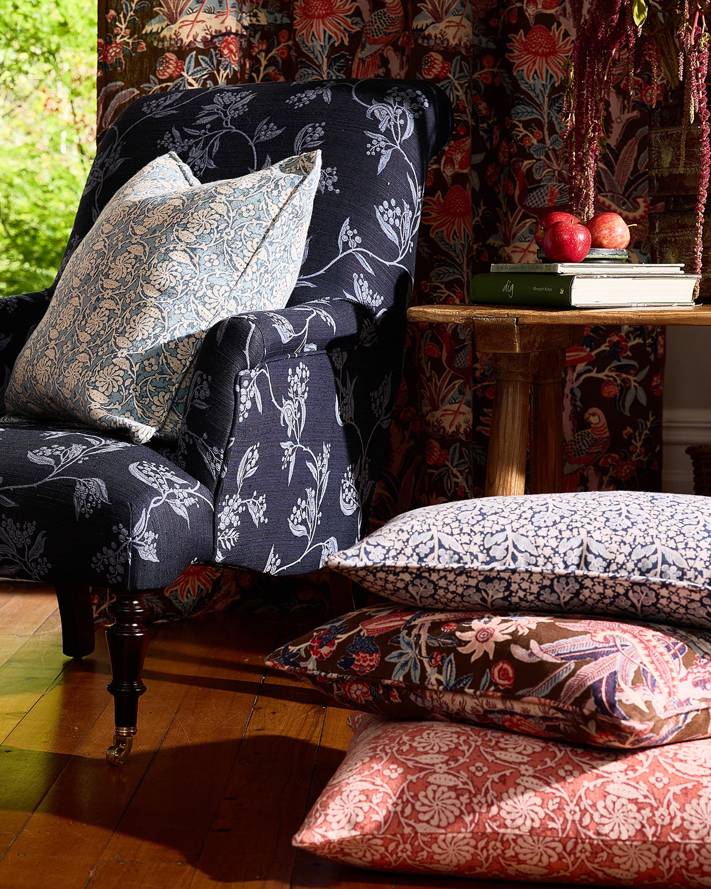 Utopia Goods: cozy reading nook with navy floral armchair, patterned cushions, side table with books and apples