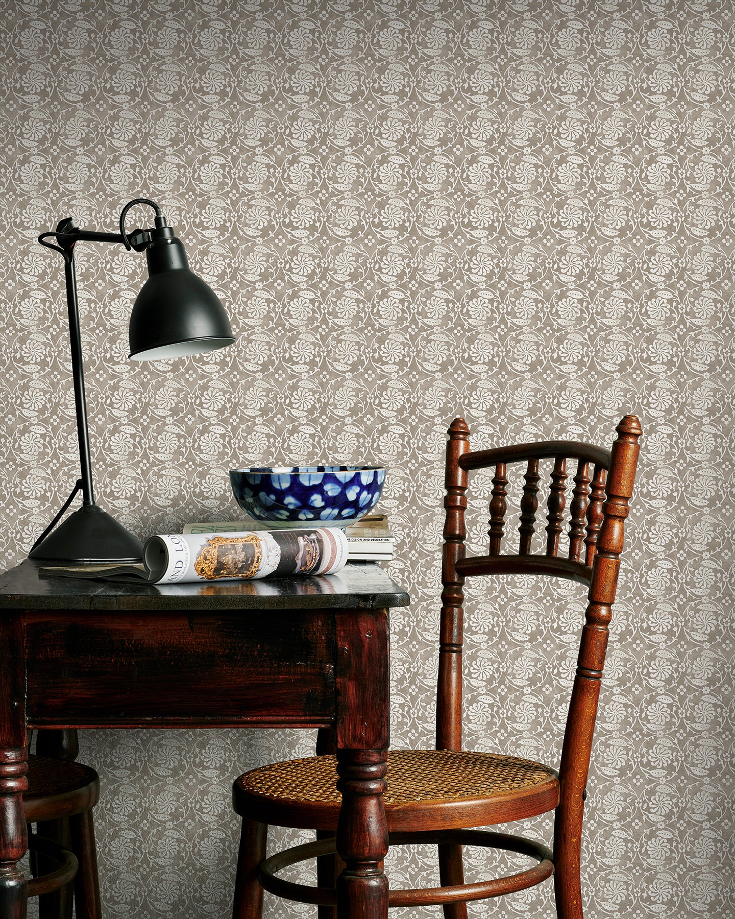 Room interior with wooden table, chair, and lamp against Utopia Goods beige wallpaper  Designer floral wallpaper Pinwheel Taupe Wallpaper