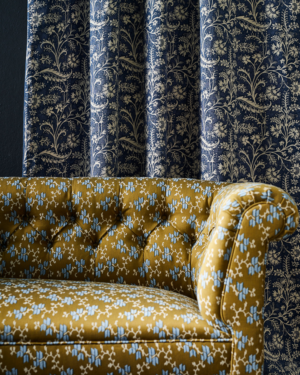 A Chesterfield sofa upholstered in Utopia Goods' Geometric Buds Khaki-Mustard perfromance fabric and Wildflower Denim curtain in the back